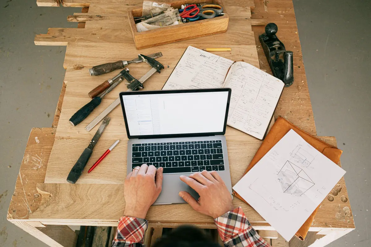 Een timmerman werkt op zijn laptop, tussen het gereedschap op de werkbank