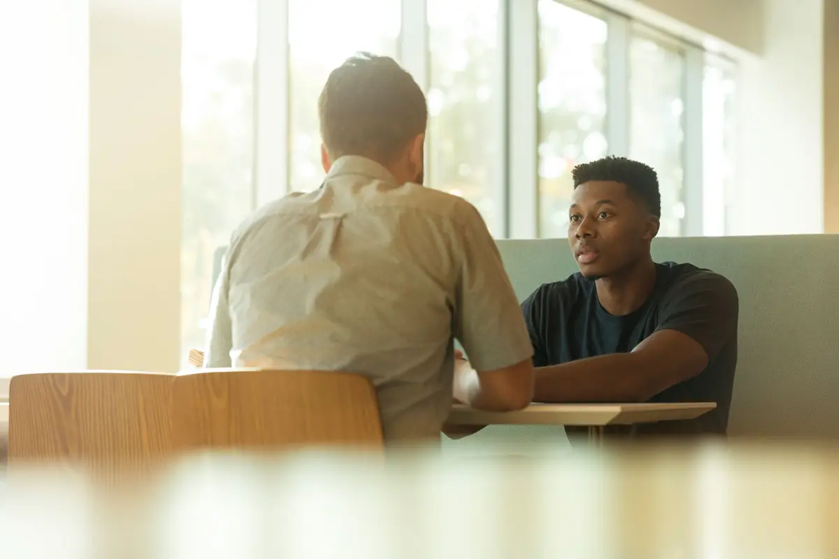 Twee mensen in gesprek aan een lichte houten tafel