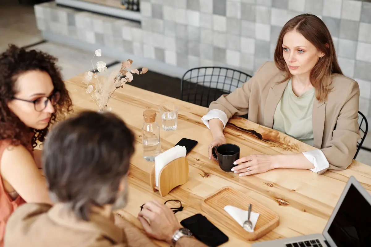 Drie mensen in gesprek aan een lichte houten tafel