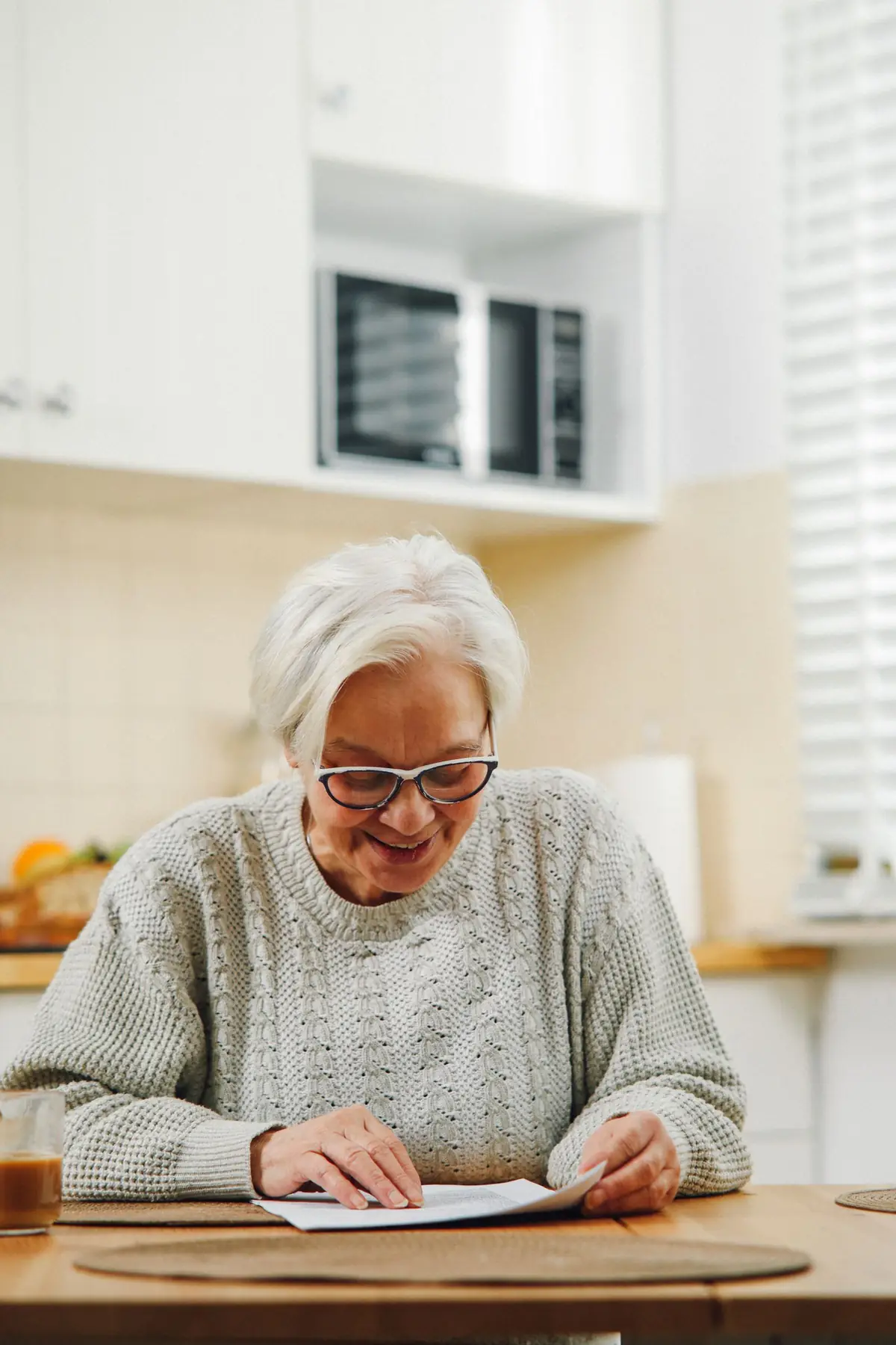 Een vrouw leest een document aan de keukentafel bij het raam